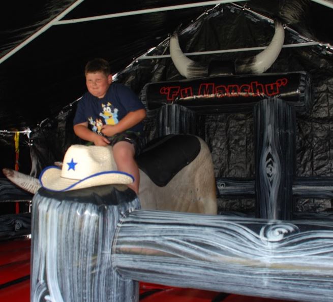 Boy riding Fu Manchu the mechanical bull, cowboy hat resting on the rail