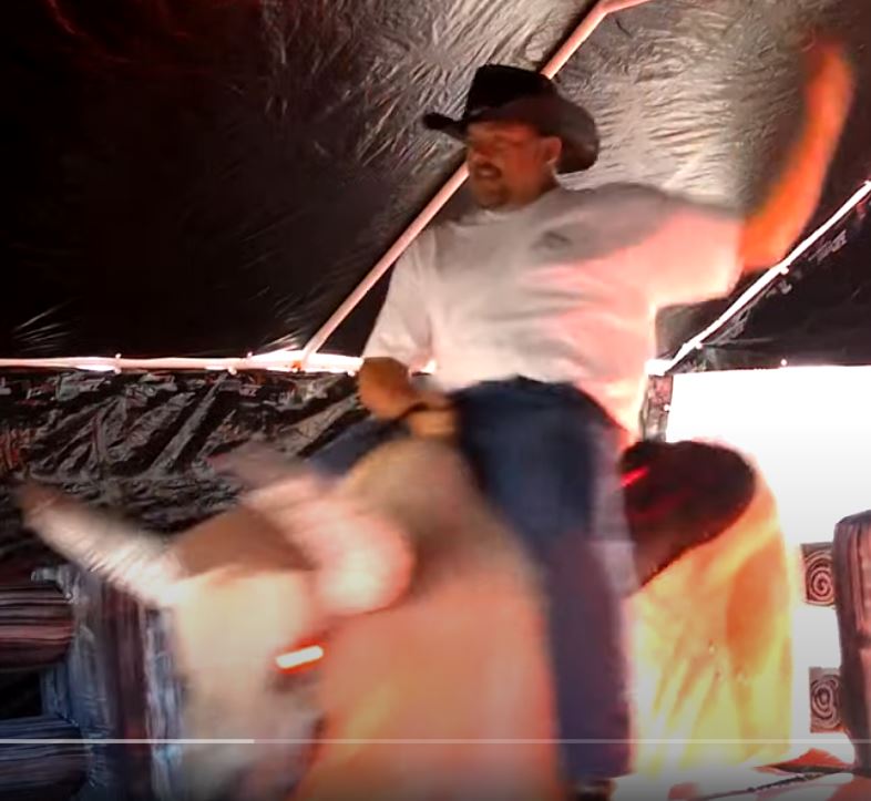 Man riding Fu Manchu the mechanical bull under the tent