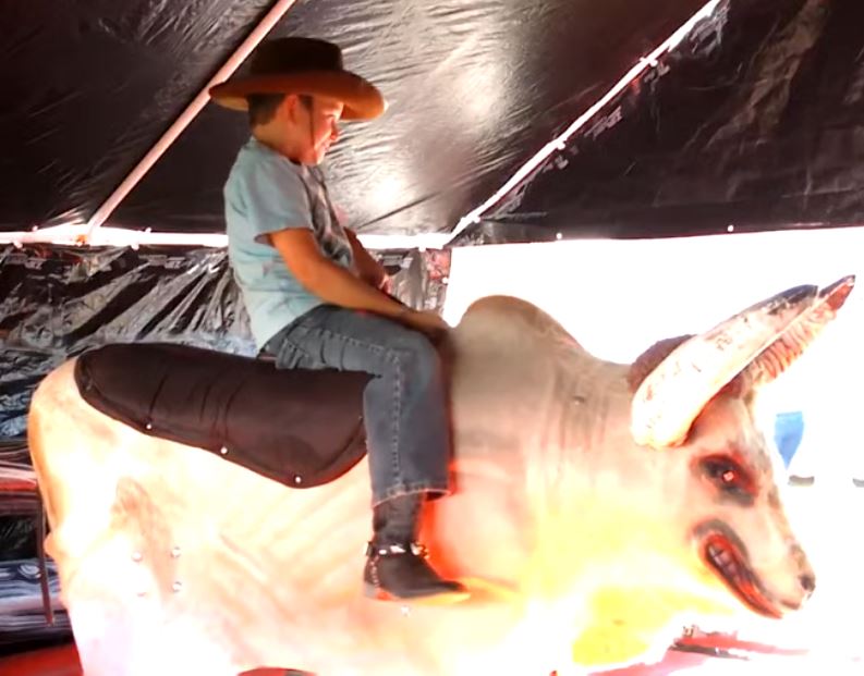 Boy riding Fu Manchu the mechanical bull under the tent