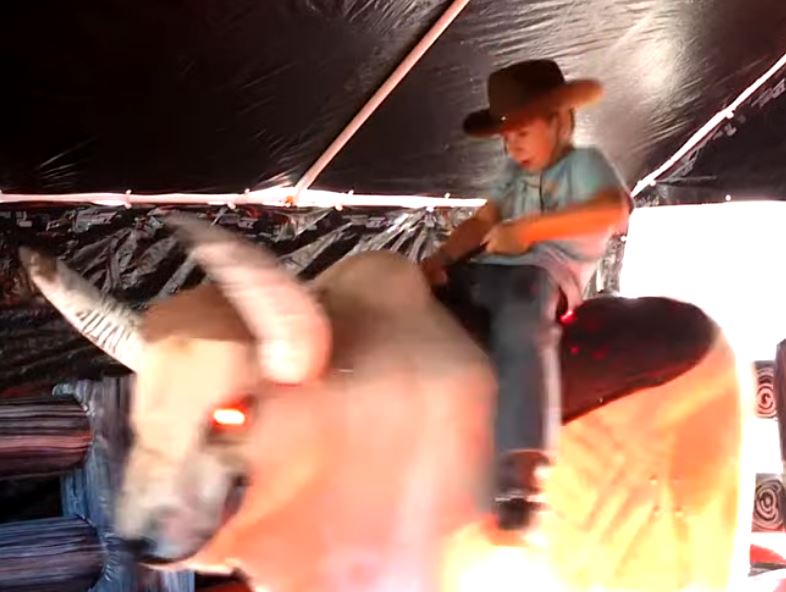 Boy riding Fu Manchu the mechanical bull under the tent