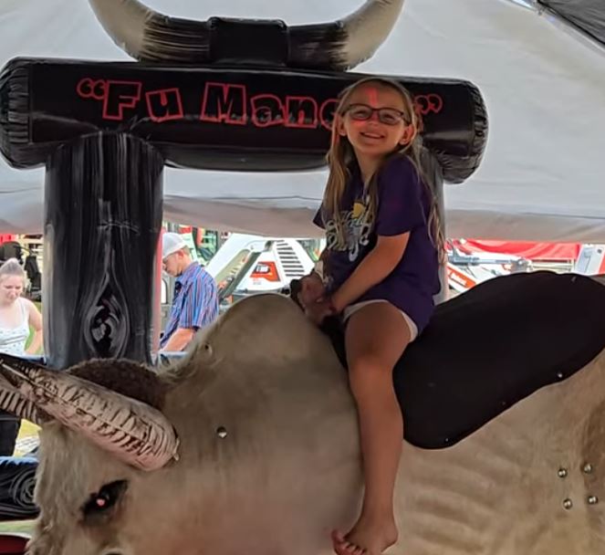 Young girl smiling while riding Fu Manchu the mechanical bull